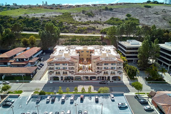 Aerial view of a multi-story building with a decorative facade and multiple balconies, surrounded by other buildings and greenery.