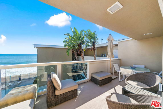 Balcony view overlooking the ocean with seating area and glass railing.