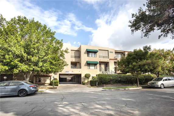 Front view of a three-story residential building with balconies and covered parking area.