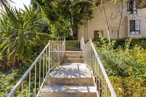 Front view of a building with stairs leading up to the entrance surrounded by greenery.