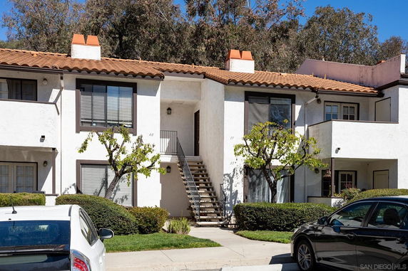 Front view of a two-story apartment building with white stucco walls and brown roof tiles.