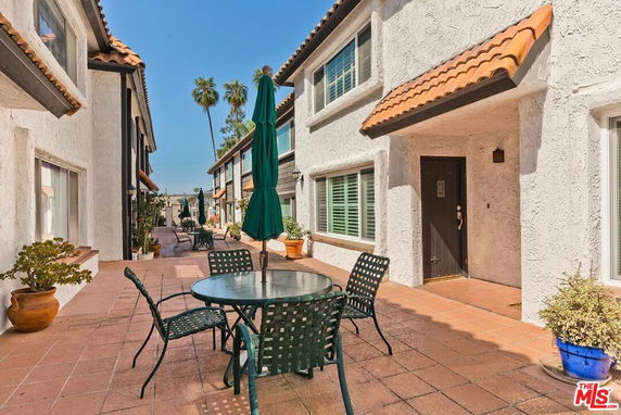 Front view of a multi-story residential building with outdoor seating area and potted plants.