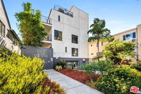 Front view of a modern multi-story apartment building with balconies and a gated entrance.