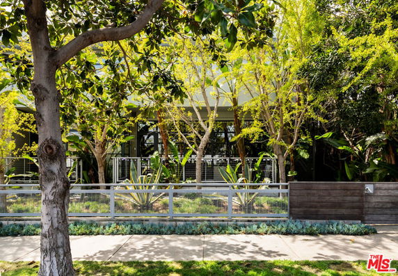 Front view of a modern house with a metal fence and trees in the foreground.