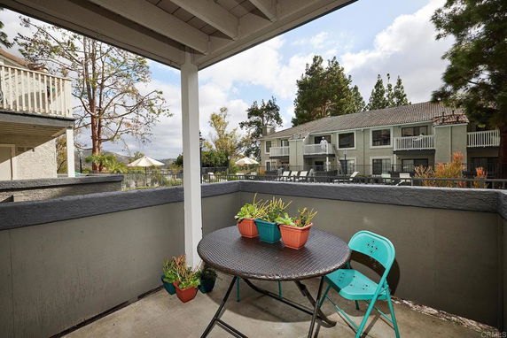 Patio area with a small table and chairs, overlooking a residential complex with multiple balcony units.