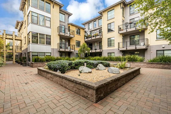 Front view of a multi-story apartment building with balconies and landscaped courtyard.