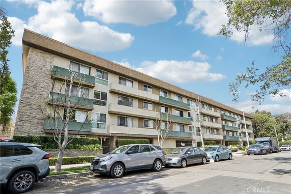 Front view of a multi-story apartment building with balconies and parked cars.