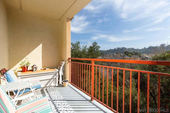 View from a balcony with outdoor furniture and railing overlooking trees and hills.