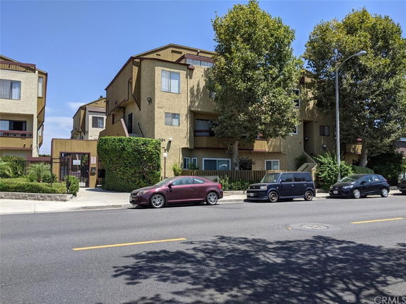Front view of a multi-story apartment building with trees and parked cars.