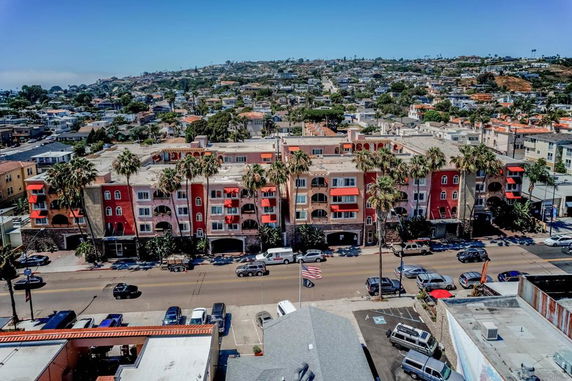 Aerial view of a colorful multi-story building with palm trees lining the street in an urban area.