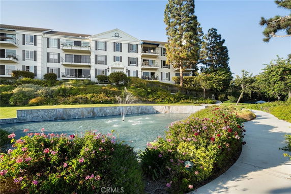 Front view of a multi-story residential building with balconies and a water fountain in front.