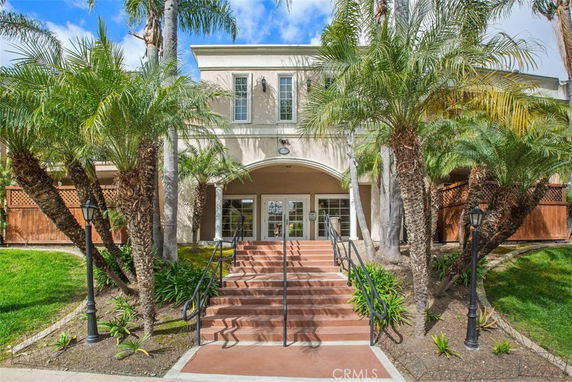 Front view of a two-story house with stairs and palm trees.