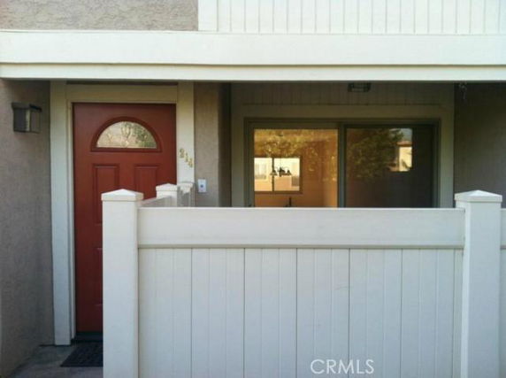 Front view of a house with a red door and fenced patio area.