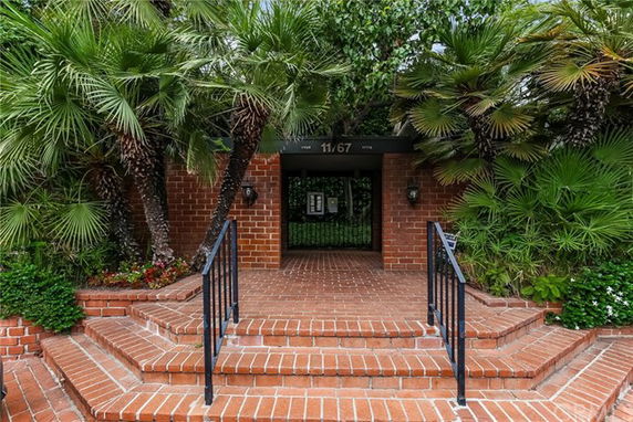 Entrance of a brick building with stairs and surrounding greenery.