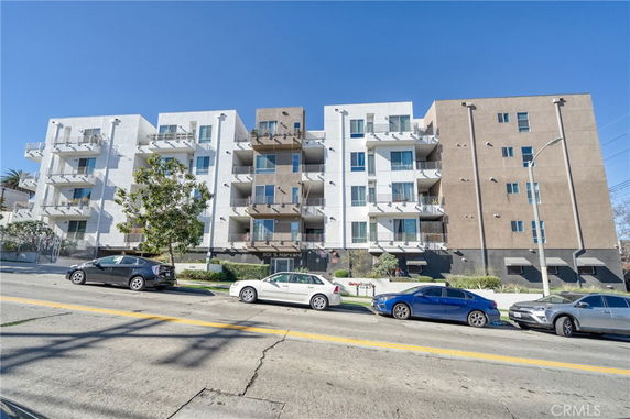 Front view of a multi-story apartment building with balconies and adjacent parking.