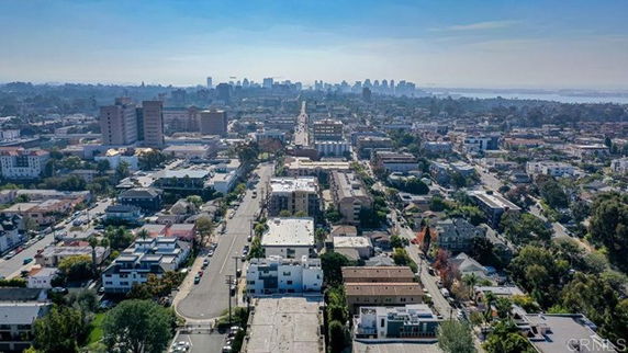 Aerial view of a cityscape with various buildings and distant skyline, under a clear sky.