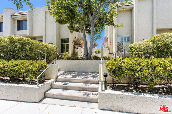 Front view of a multi-story building with stairs and greenery.