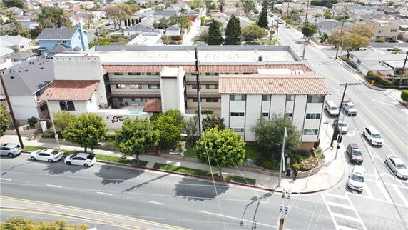 Aerial view of a multi-story residential building with a red tiled roof and white exterior walls, located at a street intersection.