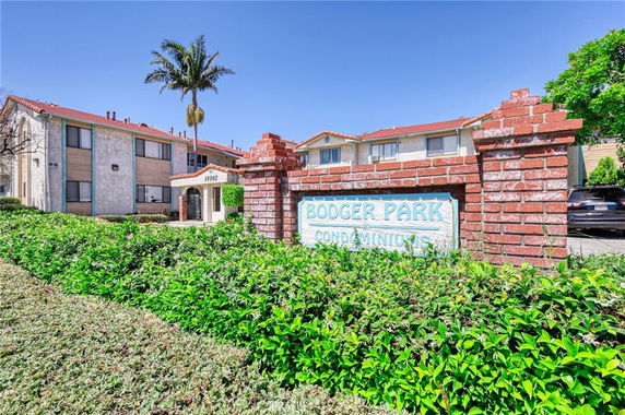 Front view of a condominium complex with a red brick sign, multiple two-story buildings, and a palm tree.