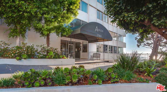 Front view of an apartment building entrance with glass doors and canopy.