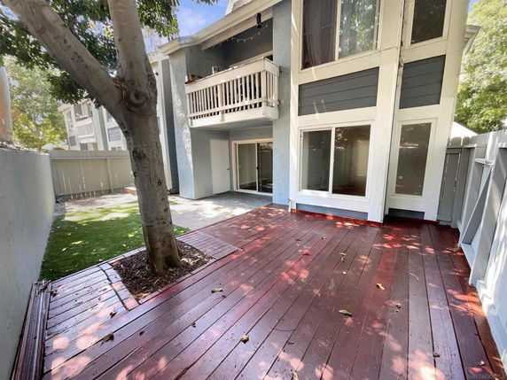 View of the exterior area with wooden deck and trees, adjacent to a multi-story building with balconies.