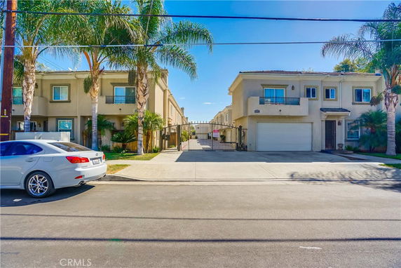 Front view of two adjacent two-story houses with palm trees in front and a gated driveway.