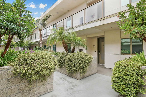 Front view of an apartment building with plants and outdoor walkway.