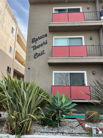 Front view of a multi-story building with balconies and vegetation in front.