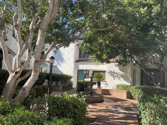 Front view of a two-story house with a white exterior and a tiled roof, surrounded by trees and bushes.
