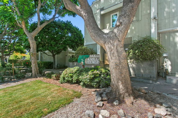Front view of a residential building with trees and a sign reading 'Oak Knoll Village.'