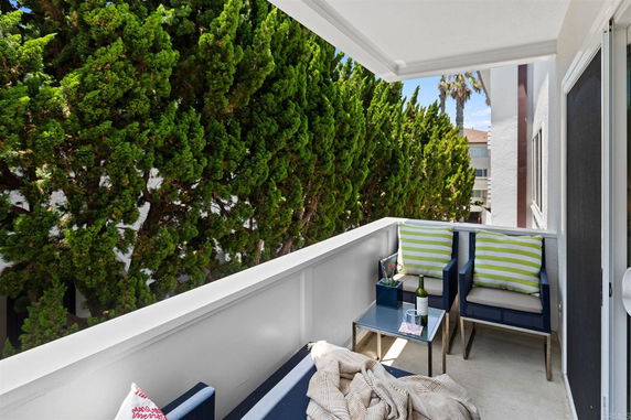 Outdoor balcony area with seating and a view of trees and neighboring buildings.