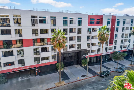 Front view of a multi-story residential building with large windows and a retail parking area.