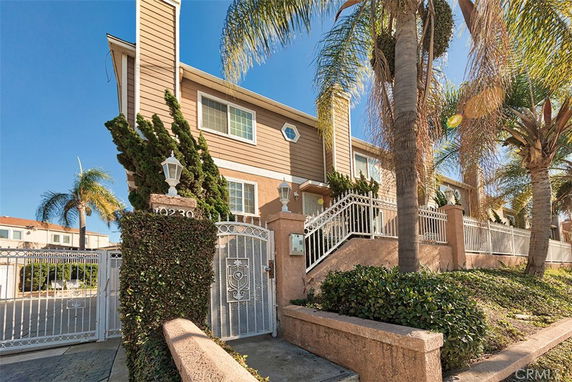 Front view of a two-story house with a large gate and palm trees.