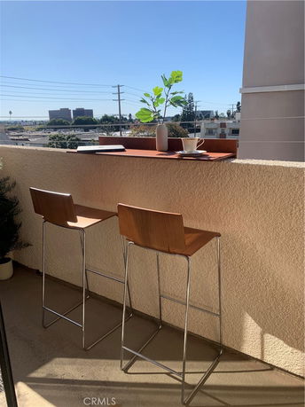 View from a balcony with two bar stools and a ledge. Urban landscape visible in the background.