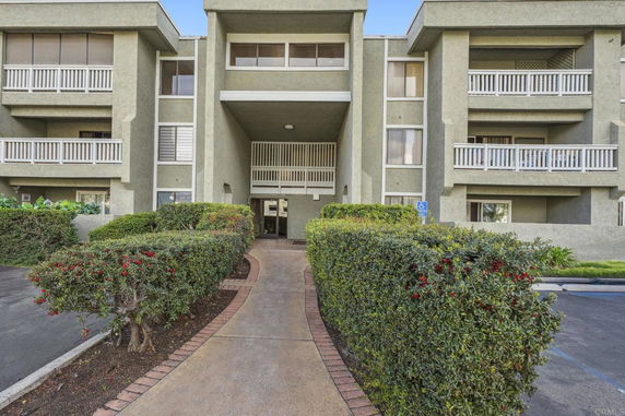 Front view of a multi-story building with balconies and a pathway leading to the entrance.