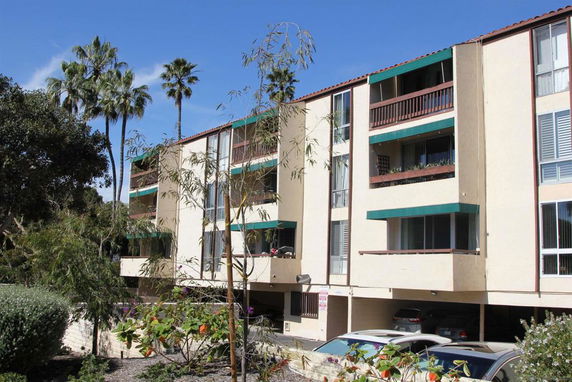 Front view of a multi-story apartment building with balconies and an open parking area.