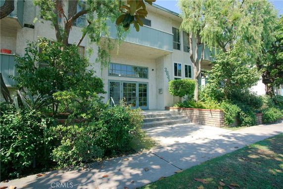 Front view of a multi-story residential building with a tree and shrubs.