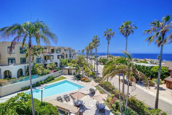 View of apartment buildings with pool area and palm trees, ocean in background
