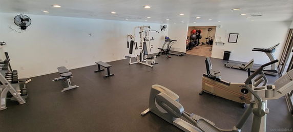Room with gym equipment including treadmills, exercise bikes, and weight machines.