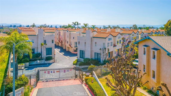 Front view of a multi-story residential complex with red-tiled roofs and gated entrance.