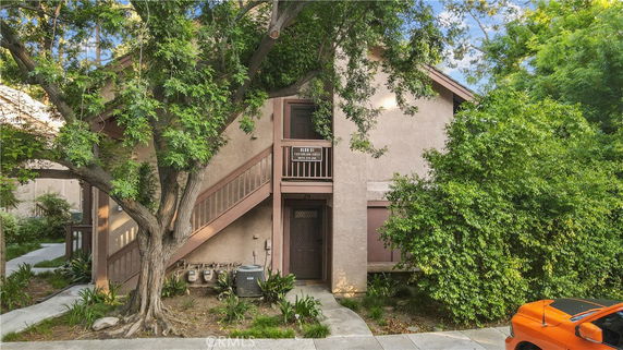 Front view of a two-story building with external staircase and foliage.