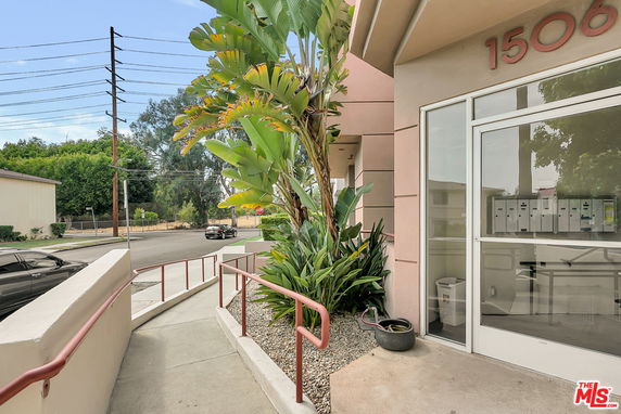 Front view of a building entrance with large windows and numbered address, surrounded by plants.