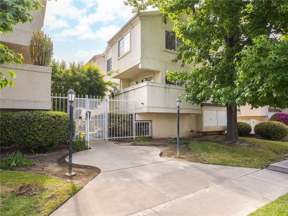 Front view of a two-story house with a gated entrance and surrounding greenery.