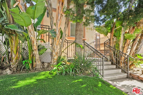 Front view of a house with a staircase leading up and surrounded by trees and plants.