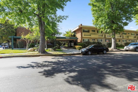Front view of a multi-story apartment building with a covered entrance and surrounding trees.