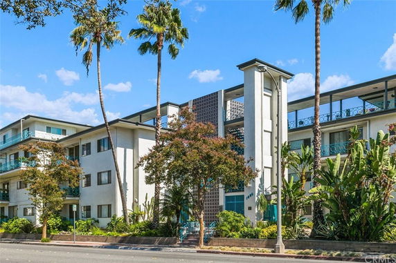 Front view of a three-story residential building with balconies and palm trees.
