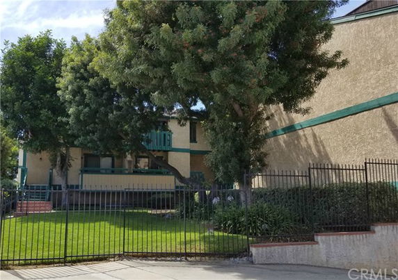 Front view of a multi-level residential building with a gated entrance and trees.