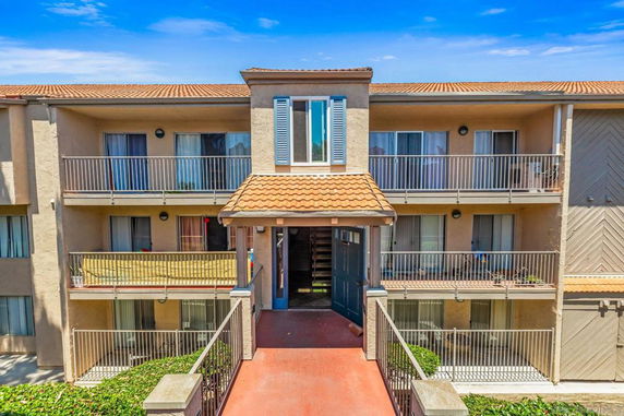 Front view of a multi-story apartment building with balconies and a tiled roof.
