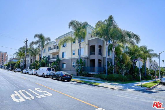 Front view of a multi-story apartment building with balconies and palm trees.