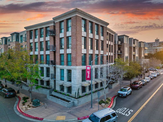 Front view of a multi-story apartment building with brick facade and large windows, along a tree-lined street.